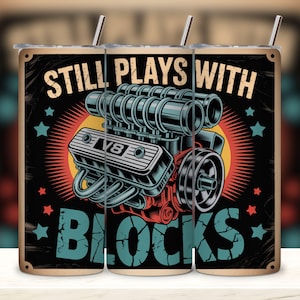 May include: A stainless steel tumbler with a retro design featuring a V8 engine illustration. The text "STILL PLAYS WITH BLOCKS" is displayed above and below the engine graphic. The tumbler includes a straw.