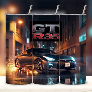 May include: A stainless steel tumbler featuring a dark gray sports car with the text "GT R35" in red and gray. The car is depicted on a wet street at night, with city lights in the background.
