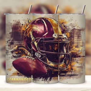 Puede incluir: Un vaso blanco con un gráfico de un casco de fútbol y un balón de fútbol. El casco es burdeos y dorado con un balón de fútbol burdeos y dorado delante de él. El texto "COMMANDERS" está en la parte inferior del vaso.