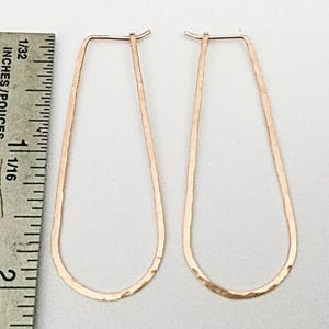 May include: A pair of long, hammered, rose gold hoop earrings. The earrings are approximately 2 inches long.