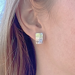 May include: Silver hammered rectangle earrings. The earrings are a light silver colour and have a textured surface.