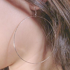 May include: Silver hoop earrings with a thin wire design. The earrings are large and circular.