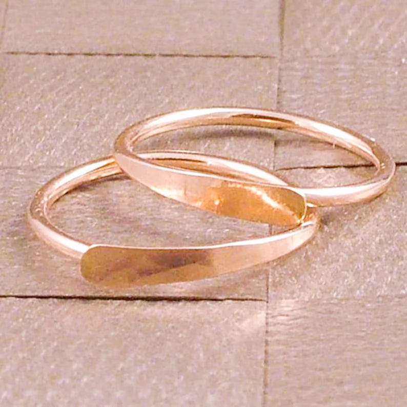 Puede incluir: Dos anillos de oro rosa con un dise&ntilde;o plano y rectangular en la parte delantera. Los anillos est&aacute;n apilados, con las secciones planas superpuestas. El fondo es una superficie texturizada y neutra.