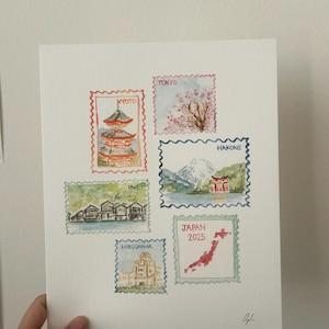 Peut inclure: Peinture &agrave; l'aquarelle repr&eacute;sentant six timbres-poste sur le th&egrave;me du Japon. Les timbres incluent des images de Kyoto, des fleurs de cerisier de Tokyo, Hakone, Ine, Hiroshima et une carte du Japon avec le texte "Japan 2025".