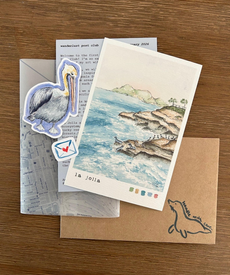 Pu&ograve; includere: Una collezione di articoli di cancelleria tra cui una stampa ad acquerello di La Jolla, un adesivo di pellicano e una busta marrone con un'illustrazione di foca. La stampa di La Jolla raffigura un paesaggio costiero con mare e scogliere.