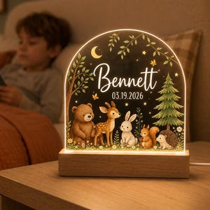 May include: An arched acrylic night light with a wooden base featuring a printed forest scene with a bear, deer, rabbit, squirrel, and hedgehog. The text Bennett and 03.19.2026 is printed in white script and sans-serif font below a crescent moon.
