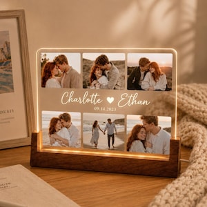 Könnte beinhalten: Ein rechteckiger Acryl-Fotorahmen mit einem dunklen Holzsockel, der sechs gedruckte Fotos eines Paares zeigt. In der Mitte befindet sich der weiße Text Charlotte, ein Herzsymbol, Ethan und das Datum 09.14.2023. Das Display wird von der Basis aus beleuchtet.