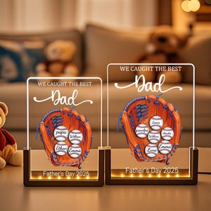 May include: Two illuminated acrylic Father's Day gifts. Each features a baseball glove with personalized baseballs and the text "WE CAUGHT THE BEST Dad". The base is dark brown with the text "Father's Day 2025".