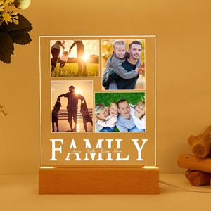 Puede incluir: Un marco de fotos de madera con un inserto de acrílico transparente que muestra cuatro fotos familiares. El marco tiene una inscripción blanca que dice "FAMILY" con los nombres Avery, Stella, Louis y Chloe debajo.