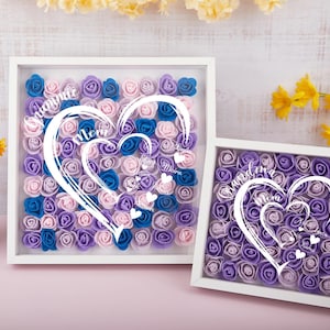 May include: Two white framed shadow boxes filled with colorful foam roses. The larger box has blue, pink, and purple roses, with a heart design and names. The smaller box has purple roses and a heart design with names.