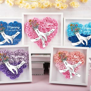 May include: Five framed heart-shaped floral arrangements in white shadow boxes. Each heart is made of small foam roses in various colors, with a hand-holding design and personalized names. The text "Mommy We Love You" is also included.