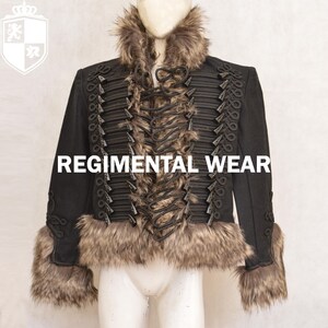 May include: A black jacket with a faux fur collar and cuffs. The jacket has a lace-up front and decorative buttons down the front. The text "REGIMENTAL WEAR" is printed on the front of the jacket.