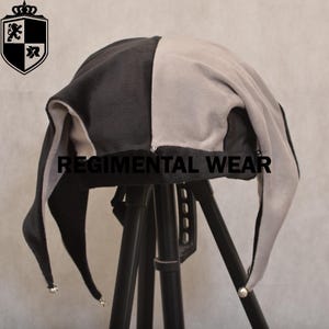 May include: A black and gray jester hat with long, pointed tips and silver bells. The hat is divided into two vertical sections, one black and one gray. The text "REGIMENTAL WEAR" is printed on the hat.