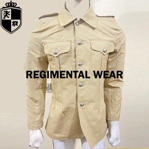Peut inclure: Veste de style militaire beige avec des boutons argentés et deux poches de poitrine. La veste a des épaulettes sur les épaules et le texte "REGIMENTAL WEAR" sur le devant. Un logo de crête est dans le coin supérieur gauche.
