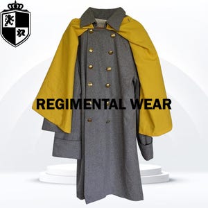 Puede incluir: Un abrigo de lana gris con forro amarillo y botones dorados. El abrigo tiene cierre de doble botonadura y cuello alto. El abrigo es de estilo militar y tiene el texto "REGIMENTAL WEAR" impreso en la parte delantera.