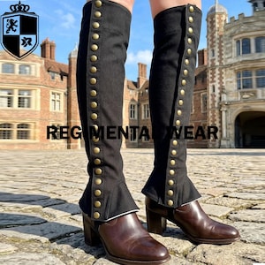 May include: Black over-the-knee boot covers featuring a vertical row of metallic gold-toned buttons along the outer side. These fabric gaiters are worn over brown leather block-heeled boots, extending from the ankle to above the knee.