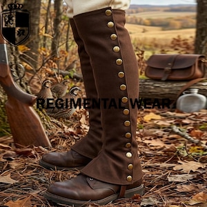 May include: A pair of brown knee-high gaiters worn over brown leather boots. The gaiters feature a vertical row of metallic gold buttons along the outer side. The text REGIMENTAL WEAR is visible in the center of the image over the forest floor.