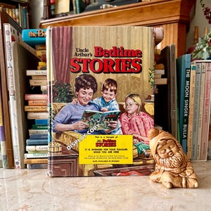 May include: A vintage copy of "Uncle Arthur's Bedtime Stories" book with a colorful illustration of a family reading. The book is displayed with other books and a small ceramic gnome figurine.