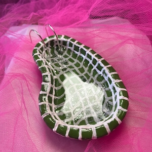 May include: A miniature, handcrafted ceramic bathtub with a green exterior and white grid pattern interior. The tub features two silver metal handles and is set against a vibrant pink backdrop. The design is whimsical and decorative.