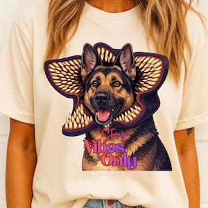 May include: Cream-colored t-shirt featuring a German Shepherd dog with a Demogorgon-inspired design around its head. The graphic includes the text "Strange Vibes Only" in a stylized font, with purple and pink accents.