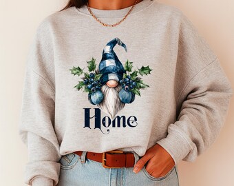 May include: A light gray sweatshirt featuring a gnome design with a blue and white plaid hat, a long white beard, and blue berry accents. The word "Home" is printed in navy blue script below the gnome.