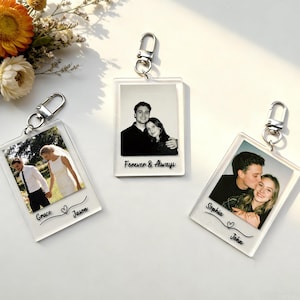 Puede incluir: Tres llaveros de acrílico transparente con cierres plateados. Cada llavero presenta una fotografía de una pareja, con nombres y frases como "Forever & Always" y "Grace & Jason". Los llaveros están sobre una superficie blanca.