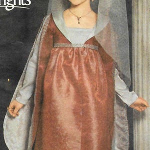 Puede incluir: Un vestido largo hasta el suelo con corpiño y falda de color óxido, mangas largas de color azul claro y un tocado a juego de color azul claro con un velo transparente. La prenda incluye un adorno plateado en la cintura y el escote, con el texto Andrea Schewe, Simplicity Trims y Rights visible en el lado izquierdo.