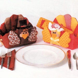 May include: Thanksgiving table setting featuring two turkey-shaped napkin holders, a white plate, cutlery, and a red napkin. The fabric napkin holders are in red, brown, yellow, and white. The plate is surrounded by a knife, fork, and spoon.