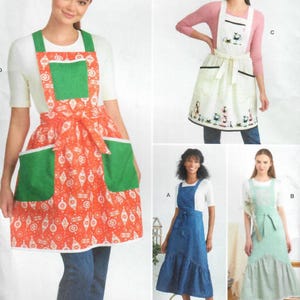 Pode incluir: A imagem apresenta quatro aventais diferentes. Um é laranja com bolsos verdes e um padrão branco. Outro é branco com uma borda preta e um desenho de gato. Os outros dois são azuis e verdes. Todos os aventais têm um design de cintura amarrada.