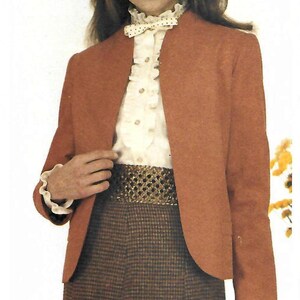 May include: A rust-colored blazer with a rounded collar is paired with a cream-colored blouse featuring a ruffled collar and cuffs. The outfit includes a patterned skirt and a gold-toned belt. The overall style is vintage.