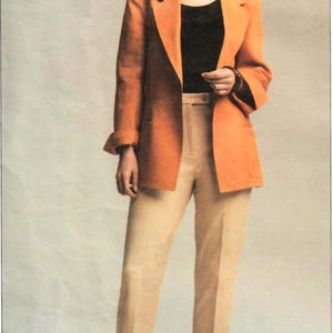 May include: A woman wearing a burnt orange blazer over a black top and tan pants. The blazer has a classic cut with a notched lapel. The pants are tailored with a straight leg. The outfit is completed with brown sandals.