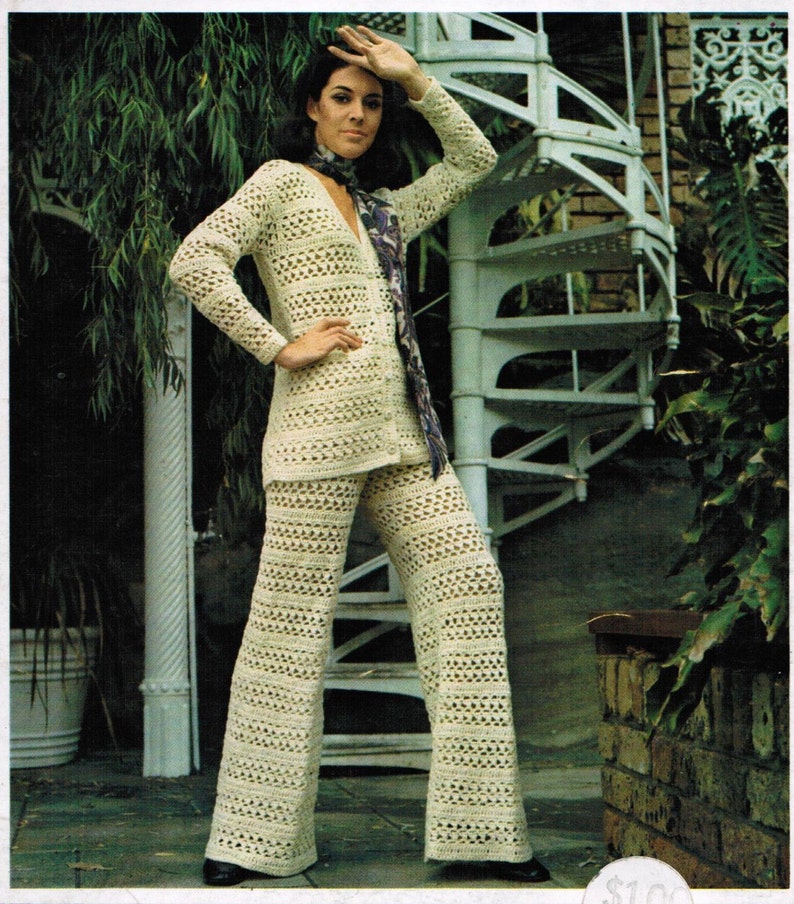 Pu&ograve; includere: Un completo pantalone in crochet bianco con un cardigan a maniche lunghe e pantaloni larghi. La modella indossa una sciarpa viola.