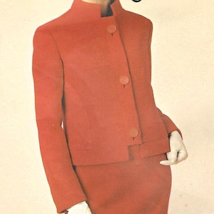 Könnte beinhalten: Vintage Modeanzeige mit einer Frau in einem roten Anzug und Hut. Der Anzug hat einen hohen Kragen und große Knöpfe. Der Text "1749 Lanvin" befindet sich oben rechts. Die Frau trägt weiße Handschuhe und Ohrringe.