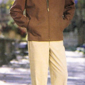 Könnte beinhalten: Eine braune Jacke mit Reißverschluss, Kragen und Seitentaschen, getragen über einem grauen Shirt, kombiniert mit einer cremefarbenen Hose und dunklen Schuhen. Die Jacke ist mit dem Buchstaben C und die Hose mit dem Buchstaben F markiert.