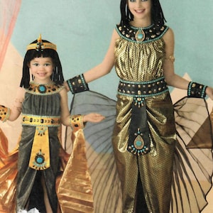 Pode incluir: Dois trajes de Cleópatra. O traje adulto é dourado com detalhes em preto e turquesa. O traje infantil é cinza com detalhes dourados e turquesa. Ambos os trajes incluem tiaras e perucas pretas.