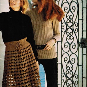 May include: Two women standing in front of a wrought iron gate. The woman on the left is wearing a black turtleneck sweater and a brown crocheted skirt. The woman on the right is wearing a beige sweater and black pants.