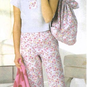 Puede incluir: Una camiseta de manga corta azul claro con un pequeño parche cuadrado, pantalones capri a juego con estampado de corazones rosas y morados, una bolsa con cordón con el mismo estampado y una manta rosa con corazones marrones. Dice easy to sew.
