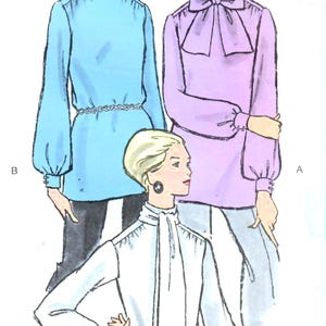 Op de afbeelding: Illustratie van drie blouses in verschillende kleuren: lichtblauw, lavendel en wit. De lichtblauwe blouse heeft een hoge hals en lange mouwen. De lavendelkleurige blouse heeft een strik bij de hals. De witte blouse heeft een stropdas en een riem.