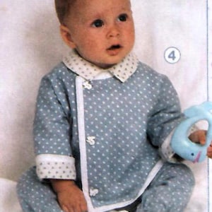 Può includere: Un bambino indossa un pigiama azzurro a pois bianchi con finiture bianche e colletto bianco. Il bambino tiene in mano un giocattolo blu. Il pigiama ha bottoni bianchi e polsini con un motivo a stelle bianche.