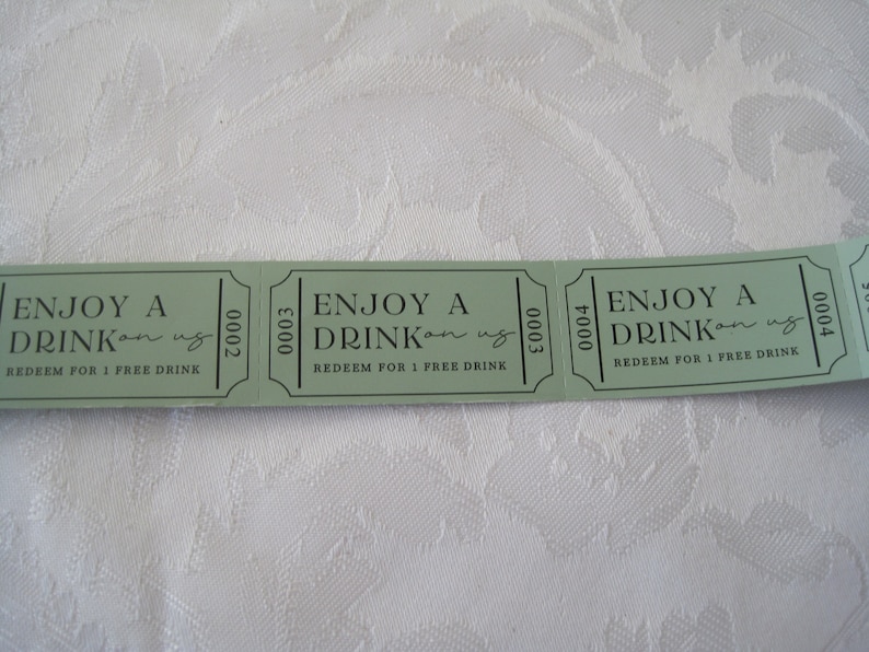Puede incluir: Tres tickets de bebida de papel verde con el texto "ENJOY A DRINK on us" y "REDEEM FOR 1 FREE DRINK". Los n&uacute;meros de los tickets son 0002, 0003 y 0004.