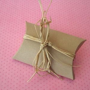 May include: A brown paper gift box tied with a natural straw bow on a pink polka dot background.