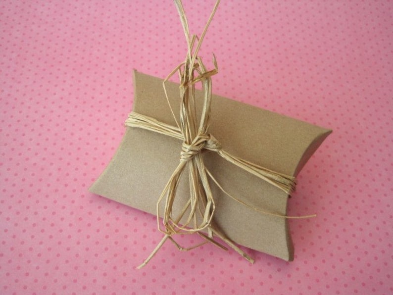 May include: A brown paper gift box tied with a natural straw bow on a pink polka dot background.