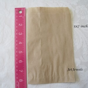 May include: A brown paper bag measuring 5x7 inches. The bag is flat and has a fold at the top. The text "Jet Jewels" is printed on the bag.