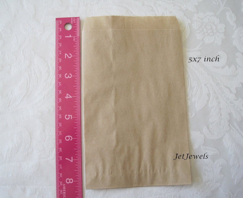 May include: A brown paper bag measuring 5x7 inches. The bag is flat and has a fold at the top. The text "Jet Jewels" is printed on the bag.
