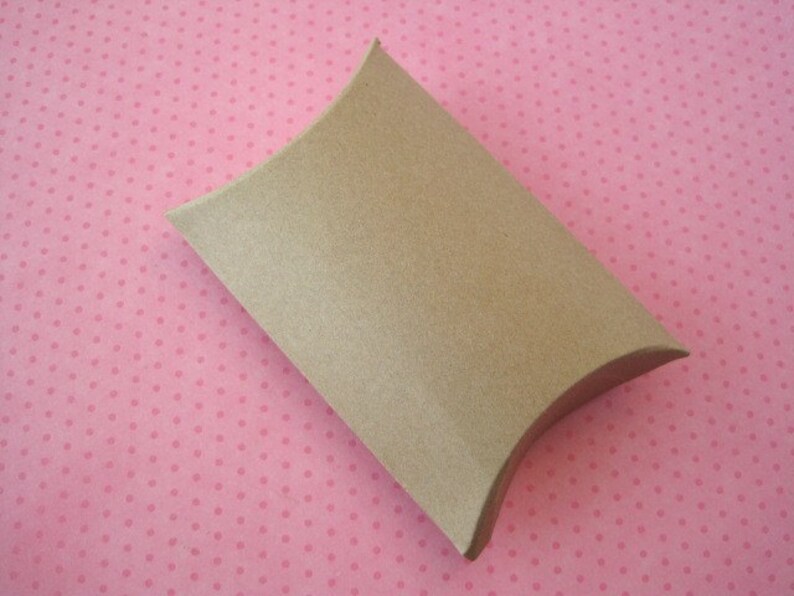 May include: A brown cardboard pillow box with a curved shape. The box is on a pink background with white polka dots.