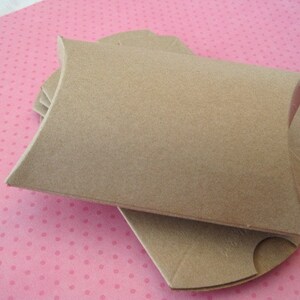 May include: A stack of brown cardboard pillow boxes. The boxes are folded and ready to be used for packaging small items.