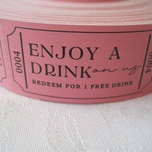 Op de afbeelding: Roze rol met tickets met de tekst "ENJOY A DRINK on us" en "REDEEM FOR 1 FREE DRINK".
