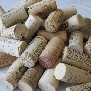 May include: A collection of used wine corks, featuring various brands and winery names printed on the ends. The corks are made of natural cork material and vary in color from light beige to dark brown.