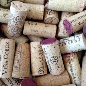 May include: A collection of used wine corks, featuring various brands and designs. The corks are primarily beige with some having purple-stained ends. Text and logos are printed on the corks, showcasing wineries and vineyards.