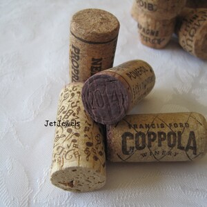 May include: A collection of used wine corks. One cork has musical notes, another has the year "2014" stamped on it. The corks are made of natural cork material and feature various winery names and designs.